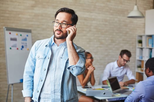 Asian businessman in eyeglasses speaking on cellphone in working environment