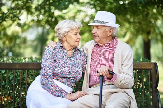 Restful seniors in smart casual sitting on bench in park and talking