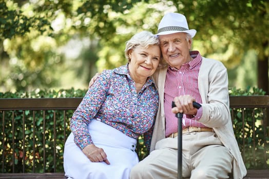 Senior couple sitting on bench in park and looking at camera