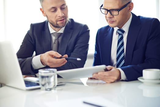 Two elegant men using digital tablet at meeting