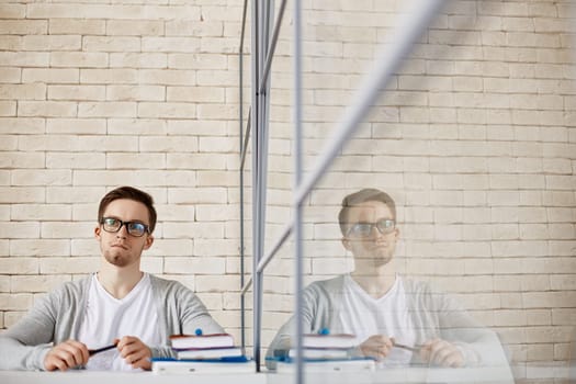 Pensive male employee in eyeglasses sitting in office