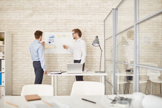 Young businessman pointing at document on board while explaining data to colleague