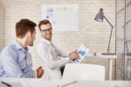 Successful businessman pointing at document with chart while looking at his co-worker