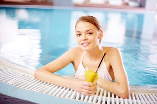 Happy girl with glass of juice looking at camera in swimming pool
