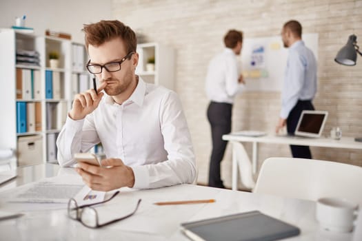 Serious businessman writing or reading sms in working environment