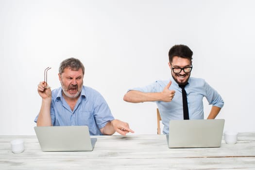 The two colleagues working together at office on white  background. both men are looking at the computer screens. a young man getting good news. the old man is upset. concept of competition in business and jealousy