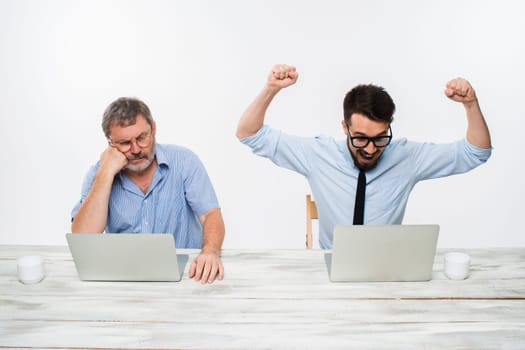 The two colleagues working together at office on white  background. both men are looking at the computer screens. a young man getting good news. the old man is upset. concept of competition in business and jealousy