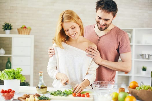 Pretty woman cutting lettuce for vegetable salad with her husband near by