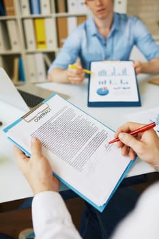 Businessman signing contract while his colleague explaining document with data