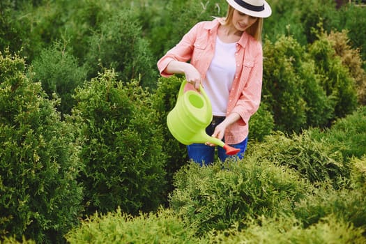 Female with water-pot watering green thuja