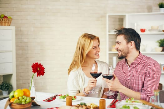 Happy young couple toasting with red wine by breakfast
