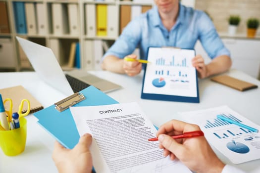 Businessman signing agreement on background of his colleague pointing at document