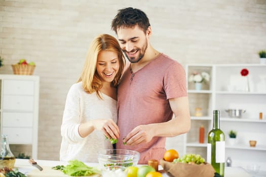 Young couple putting cut lettuce into bowl