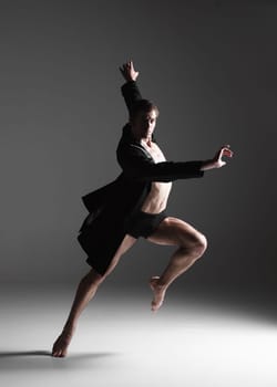 The young attractive modern ballet dancer in black jacket over white background.