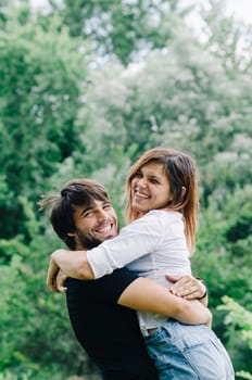 Happy couple kissing and hugging in nature. Young man and woman in loving relationship having fun in park. Boyfriend and girlfriend show emotions and caring.