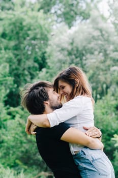 Happy couple kissing and hugging in nature. Young man and woman in loving relationship having fun in park. Boyfriend and girlfriend show emotions and caring.