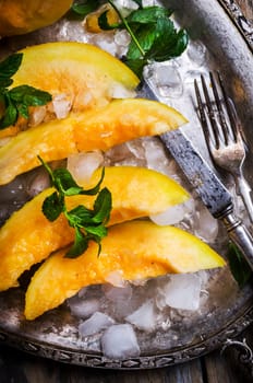 Top view of cantaloupe melon slices with mint and ice served  on vintage sliver plate. Sweet fruit dessert still life from above.