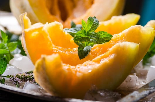 Closeup of cantaloupe melon slices with mint and ice served  on vintage sliver plate. Sweet fruit dessert still life.
