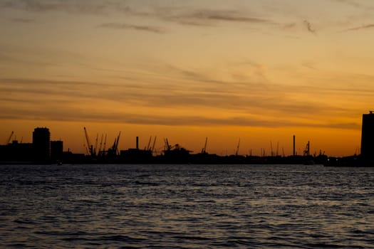 Silhouette of Rotterdam port in the Netherlands during an orange sunset.