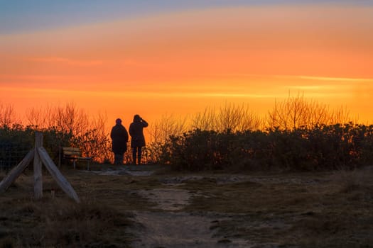 The dark silhouettes of 2 people watch the orange sunset on the beach of Rügen on the Baltic Sea.