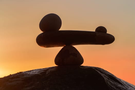 in the balance of power - natural scales of stones by the sea to the orange sunset - symbol photo