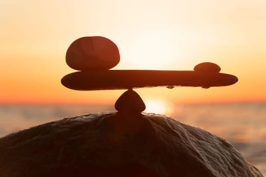 in the balance of power - natural scales of stones by the sea to the orange sunset - symbol photo
