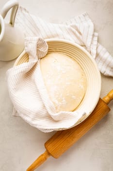 Raw yeast dough resting and rising in a special basket on kitchen table