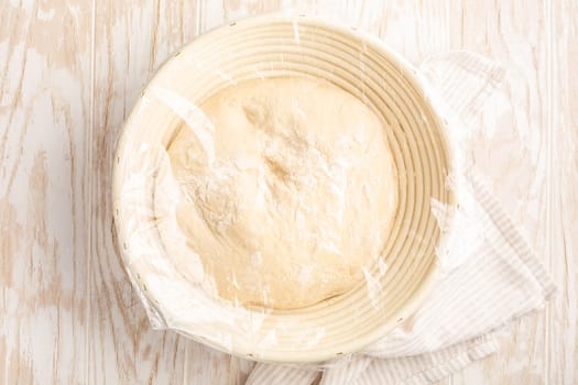 Raw yeast dough resting and rising in a special basket on kitchen table