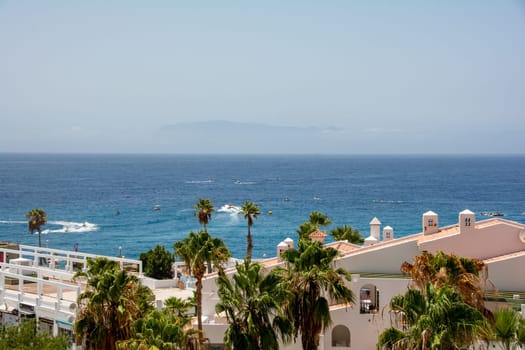 Bungalows and palm trees by the sea on the Canary Island of Tenerife in Costa Adeje in Spain. The island of La Gomera can hardly be seen on the horizon because of haze