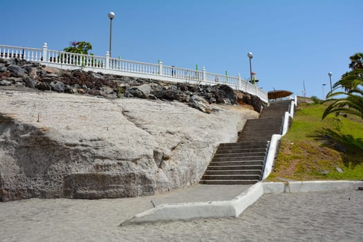 Stairs to the Torviscas Playa sandy beach, with palm trees and blue sky in Costa Adeje, Tenerife, Spain
