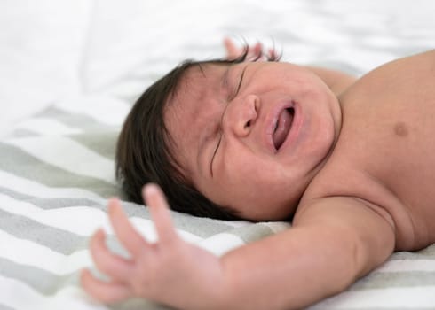 Newborn baby crying on white and grey striped blanket sheet. Infant 1 month screaming on bed. Colic and abdominal pain infant.