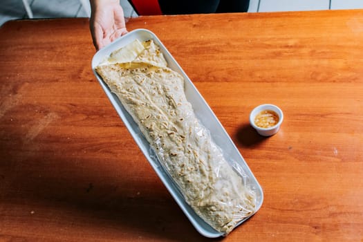 Hand holding a traditional quesillo served on wooden table. Top view of Nicaraguan Quesillo on a plate served on wooden table. Delicious traditional Nicaraguan quesillo served on wooden table