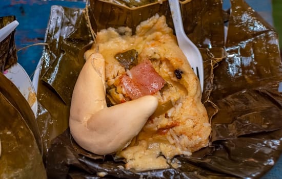 Nacatamal served with bread in a banana leaf on the table. Traditional Nacatamal served in banana leaf, Nicaraguan Nacatamal with bread on the table, Traditional Venezuelan Hallaca served