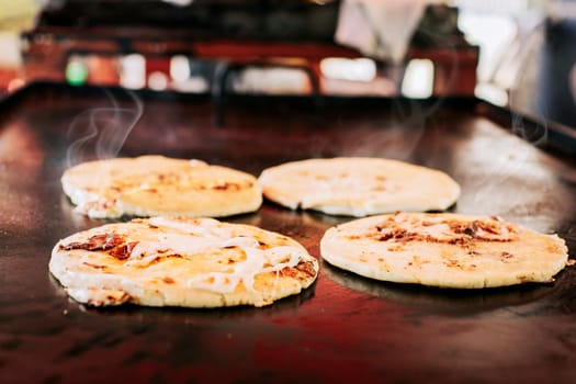 Traditional Salvadoran pupusas with melted cheese on a grill, Traditional cheese pupusas on the grill. Side view of four traditional crispy pupusas on the grill