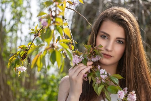 Attractive brunette girl posing on camera outdoors near sakura tree. Horizontally.