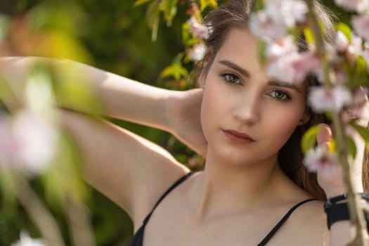 Attractive brunette girl posing on camera outdoors behind sakura tree closeup. Horizontally.