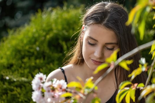 Serious beautiful girl poses behind a blossoming sakura tree.  Horizontally.