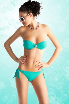 cute sexy brunette in green bikini with white sunglasses and curly hair style over white, she is in front of the camera, her face is turned on profile and she looks down at right. Her hands are both on the hips