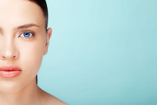 close-up half-face portrait of attractive young  caucasian  woman with pure skin over blue background