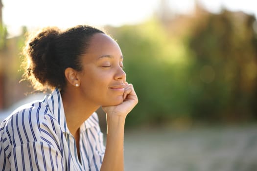 Black relaxed woman resting alone in a park at sunset