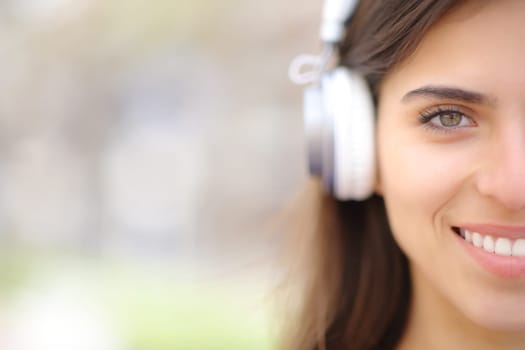 Front view portrait of a happy woman with headphone looks at you outdoors
