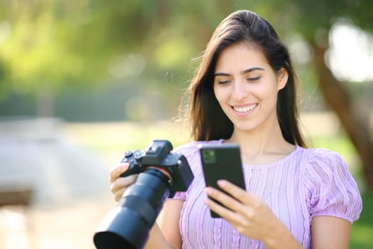 Happy photographer using phone and mirrorless camera in a park