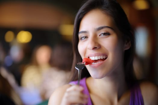 Happy woman eating strawberry in a restaurant interior and looks at camera