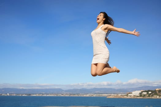 Happy woman jumping in the coast celebrating summer vacation