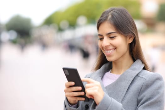 Happy woman using cell phone in winter in the street