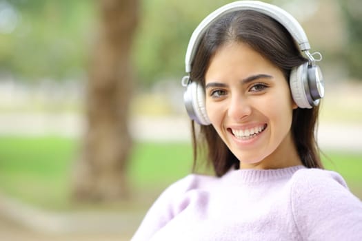 Happy woman with headphone looks at you in a park smiling