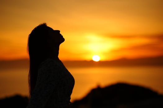 Side view portrait of a silhouette of a woman breathing at sunset or sunrise on the beach