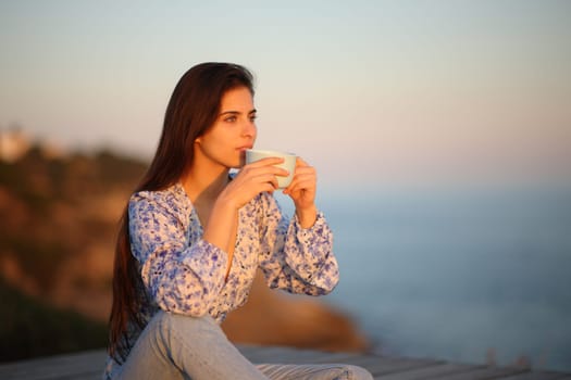 Woman drinking coffee sitting at sunset on the beach