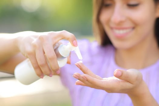 Close up portrait of a happy woman applying hydration cream on finger outdoor