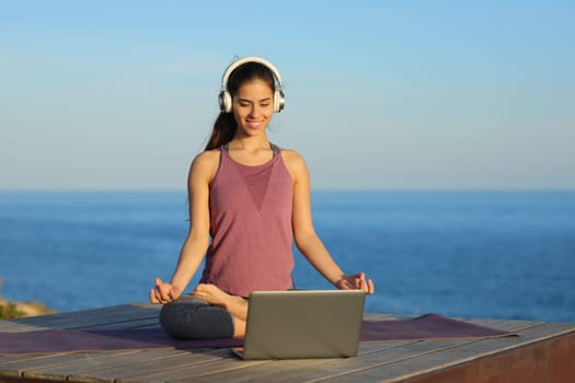 Yogi doing yoga watching video tutorial online on laptop on the beach